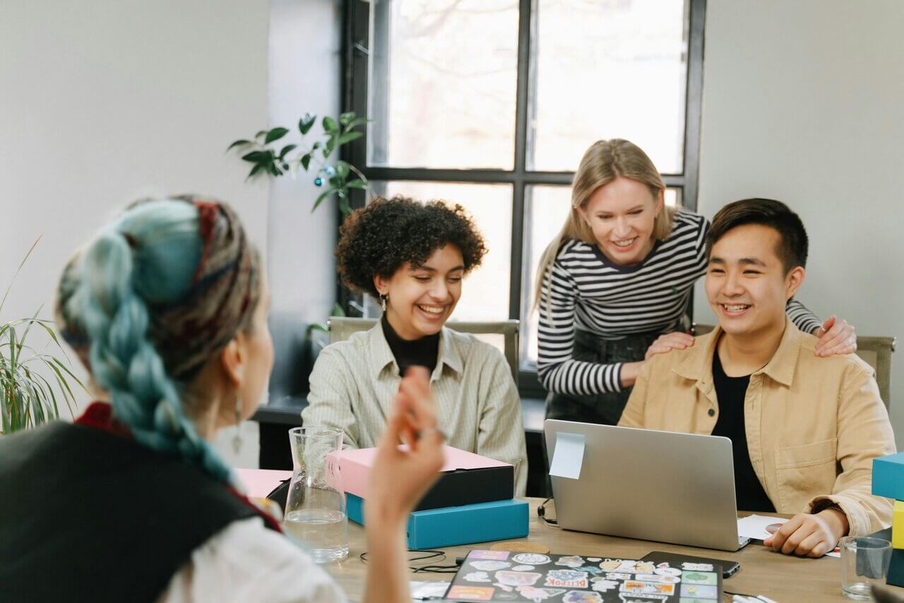 Four people sitting around a desk at work smiling 